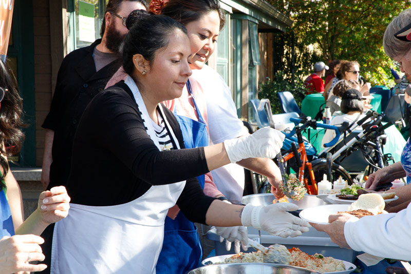 An image of people serving food to a friendly crowd,outside Mount Pleasant Neighbourhood House