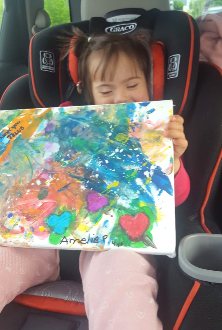 Amelie sitting in the car holding up her colourful painting