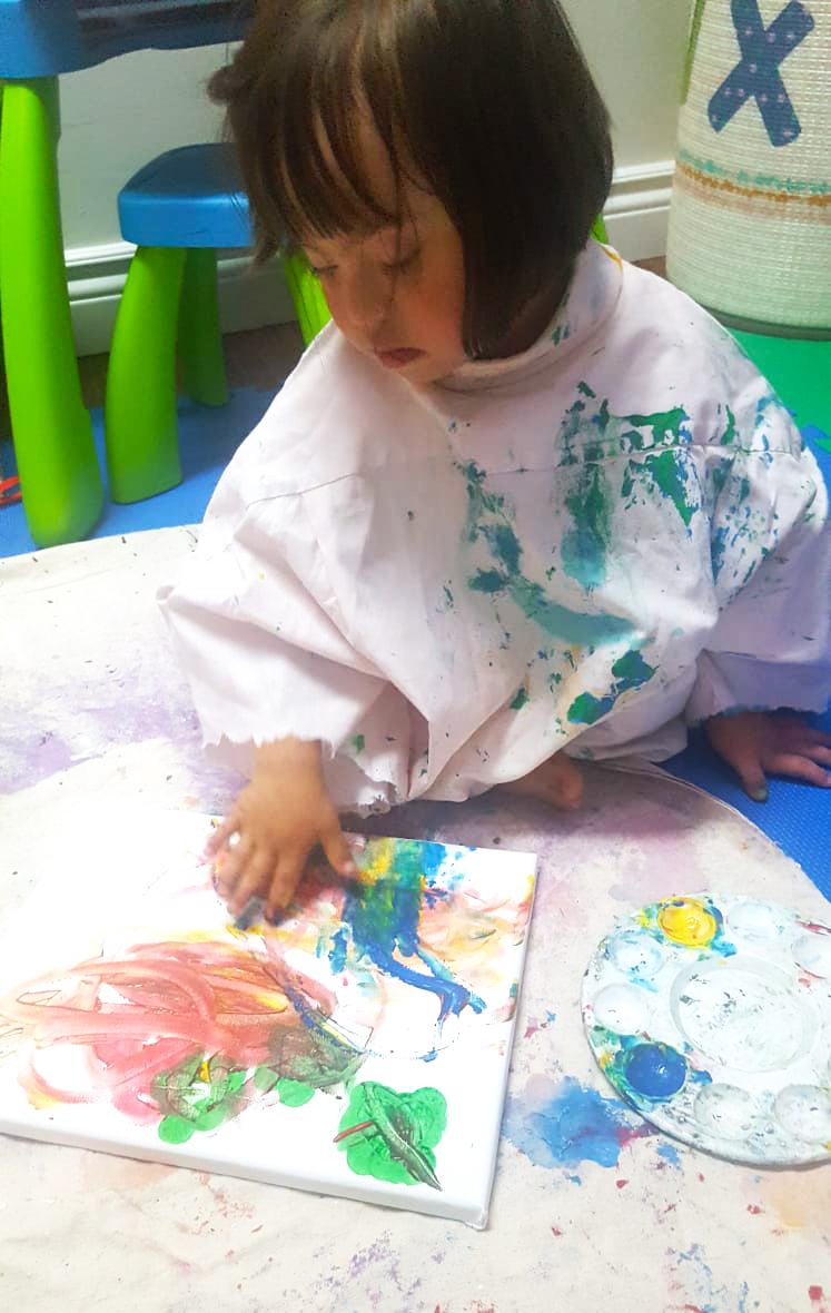 Amelie painting the artwork, daubing the canvas with bright colours
